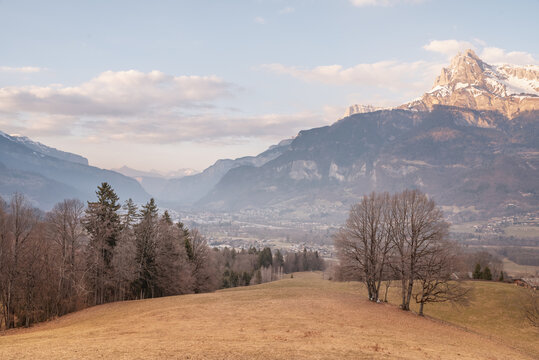 A scenic view of a small village nestled in a valley surrounded by majestic snow capped mountains