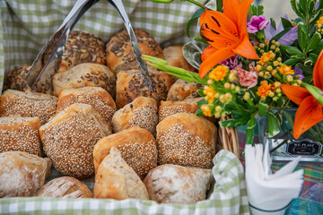 Pães rústicos de sementes e gergelim em cesta com toalha xadrez e flores