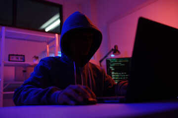 A mysterious hooded hacker working on a computer in a dark room.