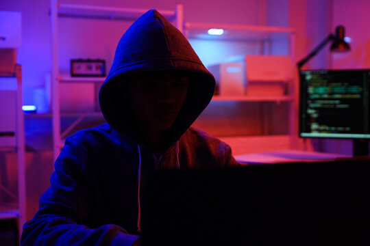 A mysterious hooded hacker working on a computer in a dark room.