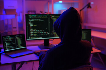 A mysterious hooded hacker working on a computer in a dark room.