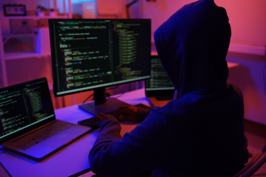A mysterious hooded hacker working on a computer in a dark room.