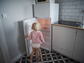 Little hungry girl looking into an empty refrigerator at home, no food concept