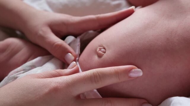 Loving mother's hands tenderly caressing and massaging her newborn baby's belly and navel to help with colic and digestion, showing a moment of care, love, and maternal connection