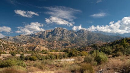 Majestic mountains rise up under a bright blue sky surrounded by lush greenery and open land.