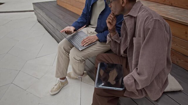 Two biracial men looking at laptop screen and gesticulating gin air while chatting about new project