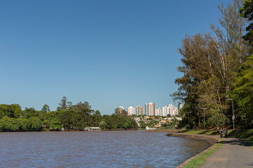 Obraz premium Orla do Lago Igapó em Londrina com caminho de pedestres e skyline ao fundo
