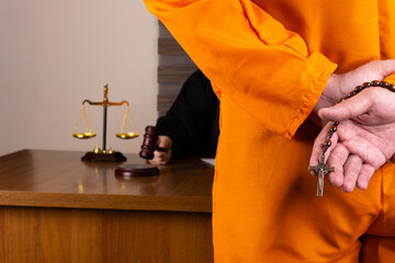 A defendant, with hands cuffed and holding a rosary, stands in a courtroom 