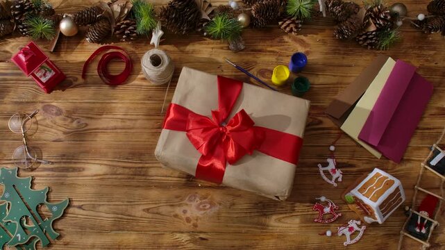 Top view of Santa Claus's gloved hands arranging festive gift boxes on a rustic wooden table. Preparations for New Year's and Christmas celebrations.