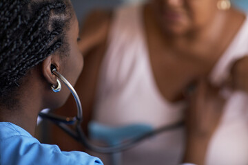 Black female young adult healthcare worker using stethoscope examining chest of middle aged female...