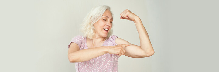 Elderly caucasian female showing strength with flexed arm in pink polka dot blouse.