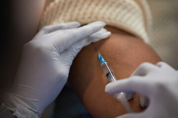 Black patient receiving vaccination in upper arm with gloved healthcare worker administering injection using syringe, close up on hands and arm, medical procedure in progress