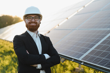 Smiling Engineer wearing white hardhat posing with arms crossed in front of solar panels