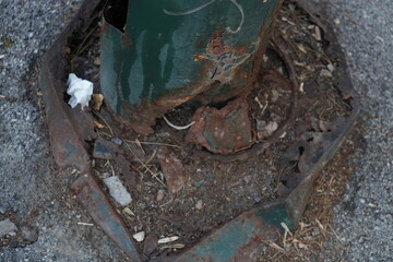 Close-up of a rusty, corroded metal post base on a city sidewalk.