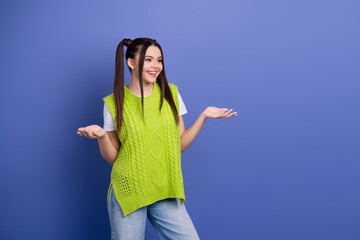 Happy young woman wearing a bright green knitted vest poses with open hands against a blue background