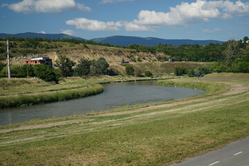 Tranquil riverside landscape with lush greenery, rolling hills, and a clear blue sky, perfect for nature and outdoor-themed visuals.