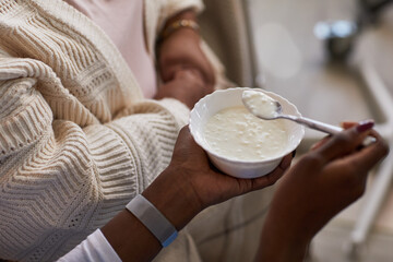 Black female nurse feeding senior woman with bowl of porridge, closeup of hands showing caregiving...