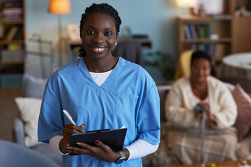 Portrait of young adult Black woman wearing medical scrubs smiling at camera holding clipboard and...
