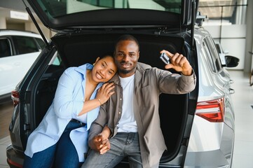 Happy african american couple showing car keys sitting in trunk at dealership