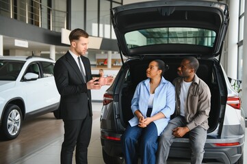 Car salesman explaining trunk features to african american couple in dealership