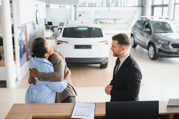 Happy African american couple hugging at car dealership after buying new vehicle