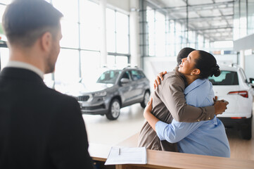Happy couple hugging after buying new car in dealership