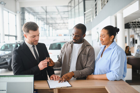 Car salesman helping couple buying new car in dealership