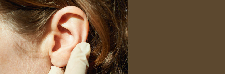 Female caucasian adult ear examined by gloved hand in medical checkup with brown hair visible.