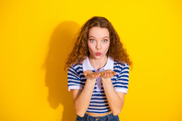 Young woman blowing a kiss against a bright yellow background in a striped polo top with casual jeans showing happiness and playful fashion vibes