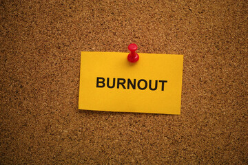 A yellow paper note with the word Burnout on it pinned to a cork board. Close up.