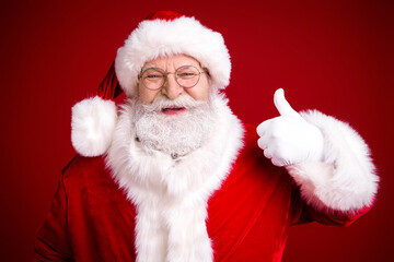 Santa Claus portrait with thumbs up in red festive suit against bold red background for christmas stock photo