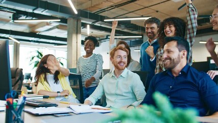 Joyful coworkers raising hands together celebrating success at workplace. Men and women laughing and cheering showing unity and motivation during team spirit moment in collaborative office environment