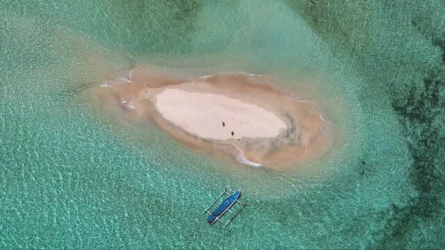 Aerial view pristine sandbar surrounded by clear turquoise water in Gili Islands of Lombok, with a traditional outrigger boat moored nearby and people exploring the small island. Tropical background