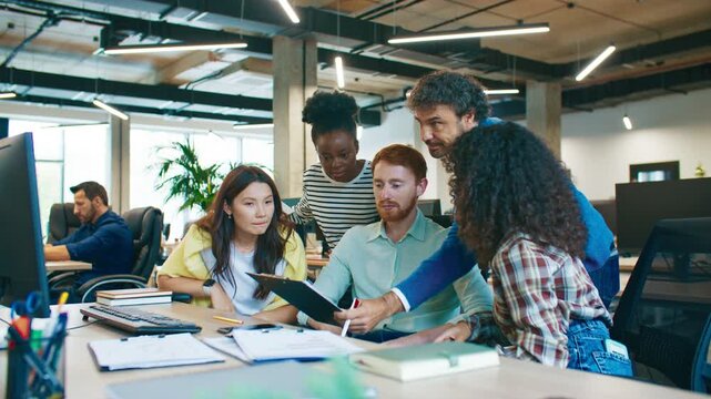 Group of coworkers analyzing printed documents together at workplace. Men and women observing charts and searching for solution to problem during discussion. Teamwork collaboration.