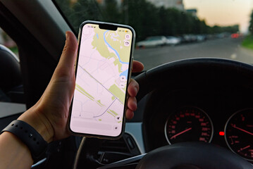 Hand holding smartphone with navigation route on screen in car an sunset.