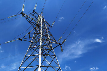 A metal pole supporting high-voltage power lines against a clear blue sky.