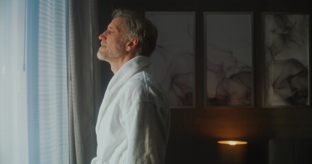 Handsome Gray Haired Man Wakes Up in Stylish Hotel Room and Opens Curtains, Filling Space With...
