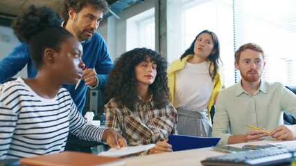 Focused group of coworkers analyzing data on monitor. Curly-haired woman pointing at screen explaining project details while teammates listening attentively and discussing ideas together in workspace.