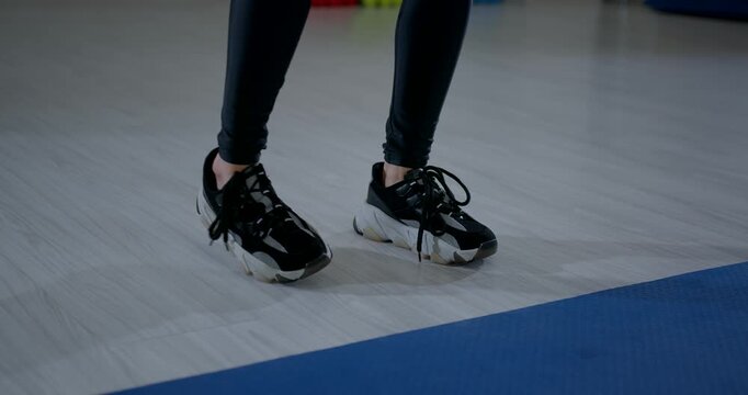 athletic woman performs heel to toe rocking exercise in a gym. She focuses on her movements while wearing comfortable workout clothes and supportive shoes.