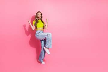Young cheerful woman in vibrant attire posing excitedly against a pink backdrop showcasing charm,...