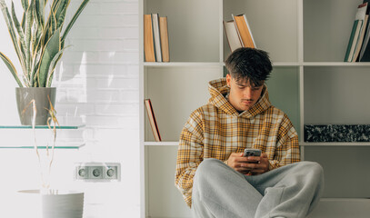 young man with mobile phone at home in casual outfit