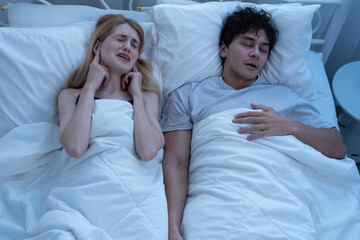 Woman covering ears with fingers while annoyed by her partner's loud snoring during night sleep, showing relationship struggles, sleep disturbance, and real-life couple issues. snoring, sleep, couple.