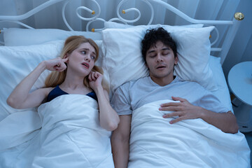 Woman covering ears with fingers while annoyed by her partner's loud snoring during night sleep, showing relationship struggles, sleep disturbance, and real-life couple issues. snoring, sleep, couple.