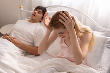 Frustrated woman sitting in bed covering her ears while her partner snores loudly, sleep disturbance, relationship issues, and frustration in a shared bedroom setting. snoring, couple, bed, sleep.