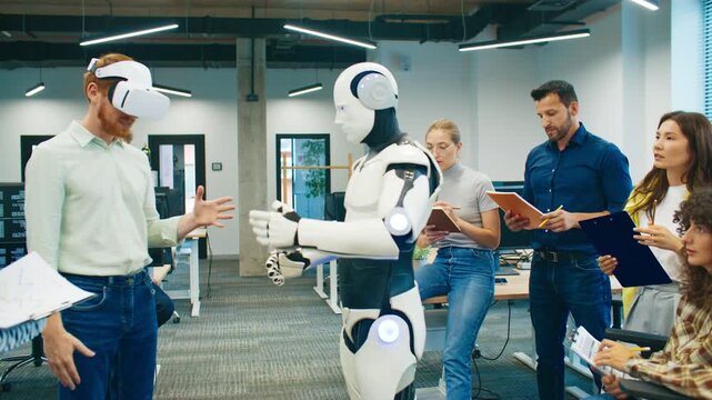 Man wearing VR headset controlling humanoid robot. Team of coworkers observing experiment and taking notes during tech presentation. Group testing innovative robotics project together in office lab.