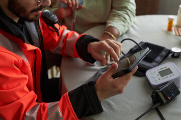 Young male paramedic wearing emergency responder uniform using digital tablet while sitting at...