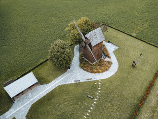 A historic wooden windmill (Franciszek) in Pępow, captured from above by a drone, surrounded by a geometric arrangement of lawns and paths, against the background of vast, green fields.