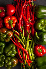Top view of red and green chili peppers with bell peppers arranged on a dark surface. Fresh organic vegetables. Spicy flavor, healthy food, and natural cooking ingredients.