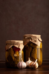 Two jars of pickled vegetables: one filled with cucumbers, the other with a colorful medley including tomatoes, garlic, and herbs. Sustainable food