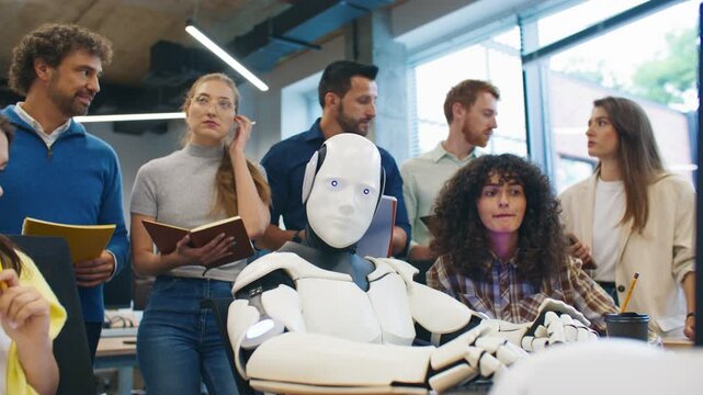 Humanoid robot sitting at computer appearing inactive while researchers observe thoughtfully. Engineering team analyzing potential malfunction or system issue during robotics experiment in lab setting